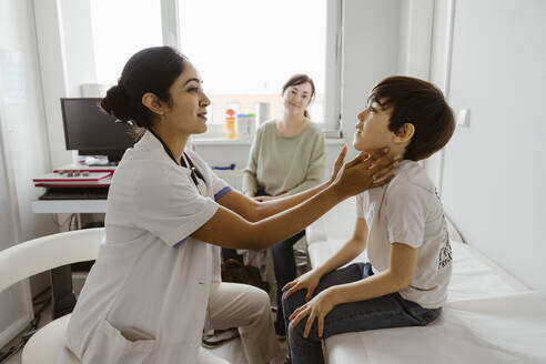Female pediatrician examining neck of boy in examination room at hospital - MASF37381