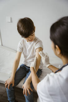 Pediatrician cleaning boy's arm with alcohol swab at healthcare center - MASF37392
