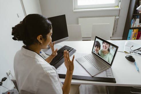 High angle view of female pediatrician waving patients over video call through laptop at desk in clinic - MASF37395
