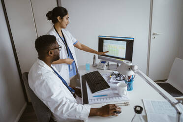 Female doctor explaining strategy to male colleague over desktop PC at healthcare center - MASF37404