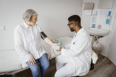 Young male doctor checking blood pressure of female patient at clinic - MASF37406