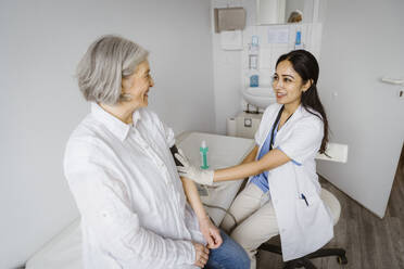 Smiling female healthcare worker consulting senior patient in examination room at clinic - MASF37408