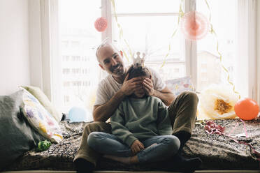 Portrait of happy man covering daughter's eyes during birthday celebration at home - MASF37413