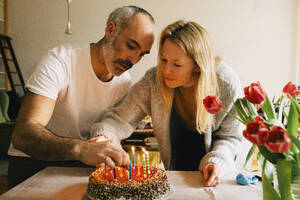 Couple arranging candles on birthday cake together at home - MASF37418