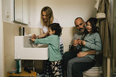 Woman helping son with washing hands while man and girl talking in bathroom - MASF37422