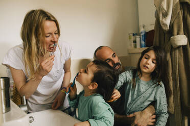 Girl combing brother's hair while he is brushing teeth with mother - MASF37423