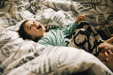 High angle view of happy boy lying on bed at home - MASF37427