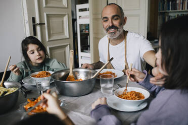Happy father eating spaghetti with children at dining table - MASF37429