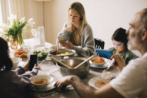 Family using gadgets while sitting at dining table - MASF37431