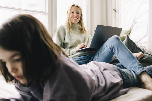 Portrait of smiling woman sitting with laptop by son at home - MASF37440