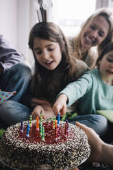 Hand of man holding birthday cake with candles against family at home - MASF37443