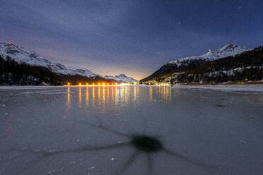 Holes in the cracked ice on Lake Champfer with Silvaplana village on background at night, Engadine, Graubunden, Switzerland, Europe - RHPLF24179