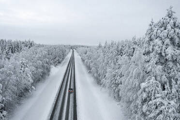 Overhead view of car driving on icy road in the snowy forest, Lapland, Finland, Europe - RHPLF24182