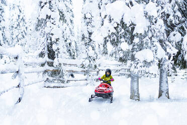 Happy young boy driving a snowmobile in the Arctic forest, Lapland, Finland, Europe - RHPLF24183