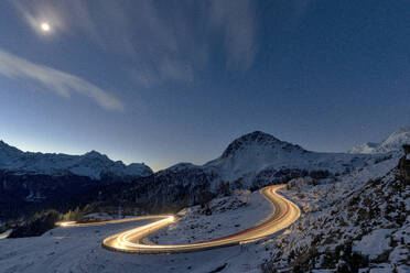 Lights of car trails on winding road covered with snow at night, Bernina Pass, Val Poschiavo, Graubunden canton, Switzerland, Europe - RHPLF24194