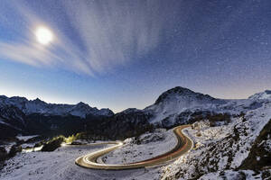 Full moon glowing over a snowy mountain road lit by car trails, Bernina Pass, Val Poschiavo, Graubunden canton, Switzerland, Europe - RHPLF24195