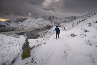 Walker on the PYG track backed by Cwm Dyli, Llyn Llydaw and Y Lliwedd in winter, Snowdonia National Park, Eryri, North Wales, United Kingdom, Europe - RHPLF24358