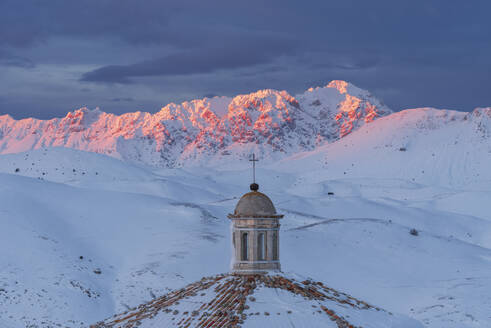 Close-up view of the roof of the church of Santa Maria della Pieta with snow covered mountains of Gran Sasso lit at sunset, Rocca Calascio, Gran Sasso e Monti della Laga National Park, Campo Imperatore, L'Aquila province, Abruzzo, Italy, Europe - RHPLF24491