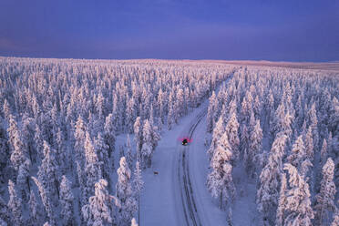 Aerial view of a car driving through the winter forest covered from snow at dawn, Akaslompolo, Kolari, Pallas-Yllastunturi National Park, Lapland region, Finland, Europe - RHPLF24505