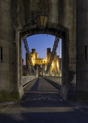 Entrance to Telford's Conwy Suspension Bridge and Conwy Castle at night, UNESCO World Heritage Site, Conwy, North Wales, United Kingdom, Europe - RHPLF24880