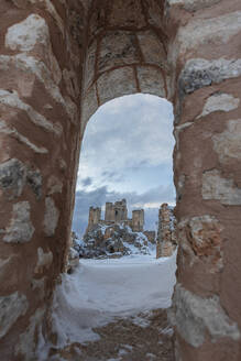 The snow covered castle of Rocca Calascio among ruins of the old village seen from an arch, Rocca Calascio, Gran Sasso e Monti della Laga National Park, Campo Imperatore, L'Aquila province, Abruzzo, Italy, Europe - RHPLF25316