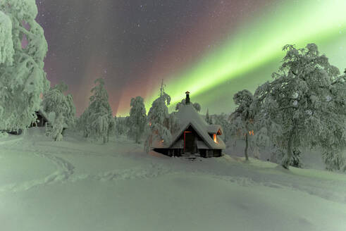Winter frame of a hut lit by the green Northern Lights (Aurora Borealis) in the icy wood with trees covered with snow, Pallas-Yllastunturi National Park, Muonio, Lapland, Finland, Europe - RHPLF25322