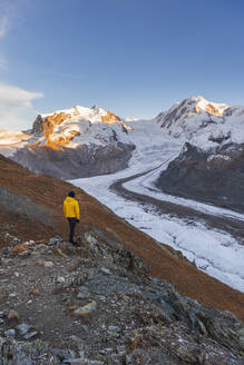 Hiker stands on rocks admiring Monte Rosa massif, Gorner Glacier (Gornergletscher) and Lyskamm peaks at sunset, Riffealp, Zermatt, canton of Valais, Swiss Alps, Switzerland, Europe - RHPLF25731