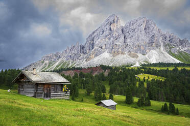 Side view of a hiker on chalet in green meadows admiring the rocky massif of Sass de Putia, Passo delle Erbe, Dolomites, Puez Odle, Bolzano district, South Tyrol, Italy, Europe - RHPLF25735