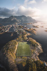Aerial view of a green soccer field on an island in the Atlantic ocean, Henningsvaer, Lofoten, Norway. - AAEF18406