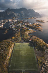 Aerial view of a green soccer field on an island in the Atlantic ocean, Henningsvaer, Lofoten, Norway. - AAEF18407