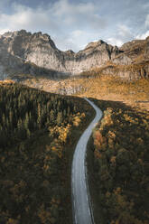 Aerial view of a winding road in a middle of nowhere enclosed by a mountain ridge at sunrise, Nusfjord, Lofoten, Norway. - AAEF18409