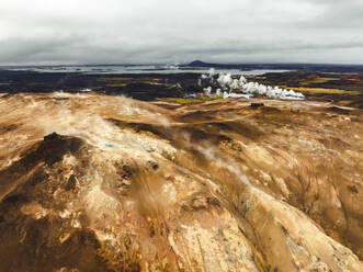 Aerial view of a volcanic hot spring with sulphuric smoke and a lake in background, Namafjall Hverir viewpoint, Northeastern Region, Iceland. - AAEF18611