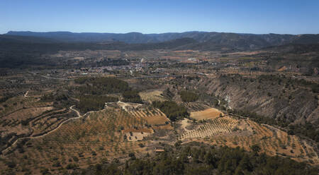 Panoramic Aerial view of a warm coloured valley with a small village with a suspended bridge standing in the middle, Calles, Valencia, Spain. - AAEF18825