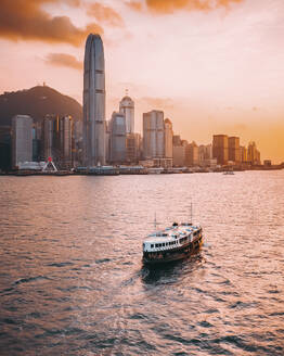 Aerial view of a passenger ferryboat along Hong Kong Island coastline at sunset with Hong Kong skyline in background, China. - AAEF18868