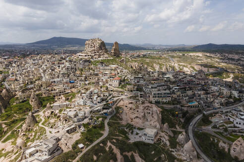 Aerial view of Uchisar, an old village huddled around the base of a huge rock cone with castle on top, Nevsehir, Cappadocia region, Turkey. - AAEF19074