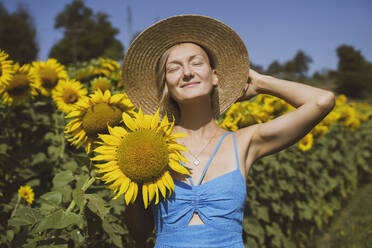 Lächelnde Frau mit Sonnenhut hält Sonnenblume im Feld - NDEF00678
