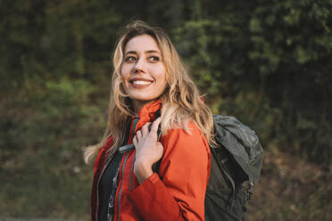 Blonde glückliche Frau mit Rucksack im Wald - NDEF00690