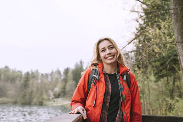 Happy woman wearing red jacket by lake - NDEF00700