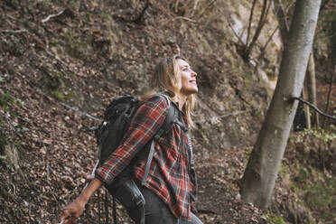 Smiling blond backpacker exploring forest - NDEF00712