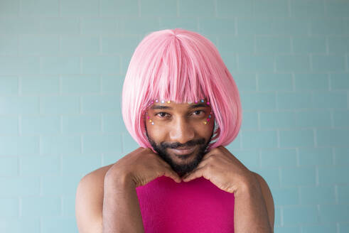 Young queer man wearing pink wig in front of tiled wall - VRAF00120