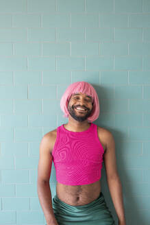 Smiling young queer man standing in front of tiled wall - VRAF00121