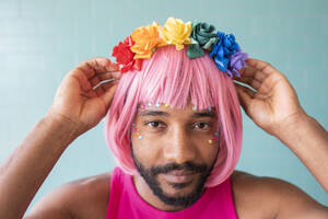 Young queer man adjusting flower tiara in front of wall - VRAF00126