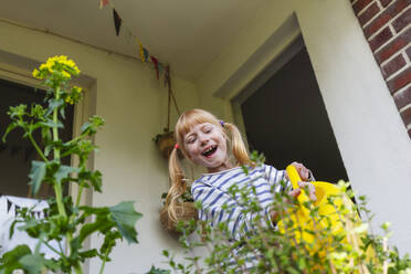 Glückliches Mädchen beim Gießen von Pflanzen auf dem Balkon - IHF01382