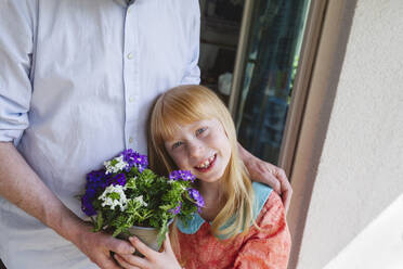 Lächelnde Tochter, die von ihrem Vater eine Topfpflanze hält - IHF01386