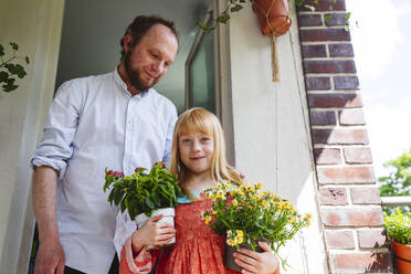 Lächelnder Vater und Tochter stehen mit Topfpflanzen auf dem Balkon - IHF01387