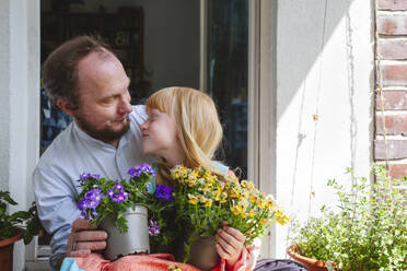 Blonde Tochter mit Vater hält Topfpflanzen auf dem Balkon - IHF01389