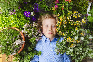 Lächelnder Junge liegt inmitten bunter Pflanzen - IHF01393