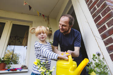 Father assisting girl watering plant in balcony - IHF01395