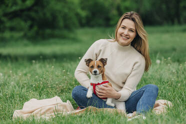 Glückliche junge Frau sitzt mit Jack Russell Terrier Hund im Park - VSNF00946