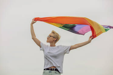 Happy woman holding rainbow flag in front of sky - VSNF00949